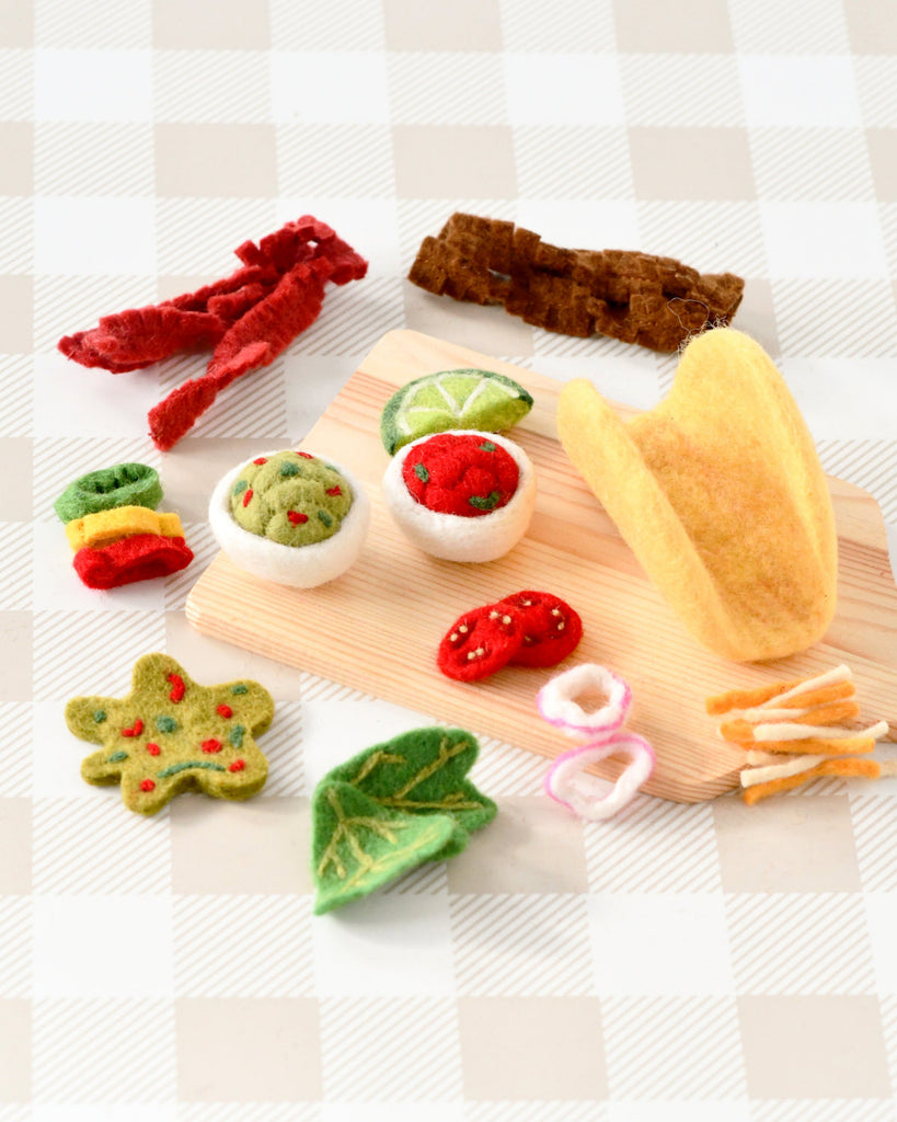 US stockist of Tara Treasures. Felt taco set with toppings on a wooden board against a checkered background