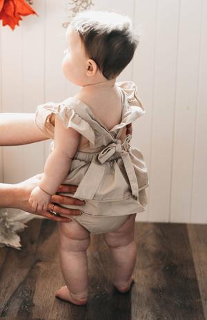 US stockist of Bencer & Hazelnut's Christmas Fir Playsuit.  Made from oatmeal colored cotton fabric, with ruffles on the back and embroidery on the front.  Snaps at crotch.