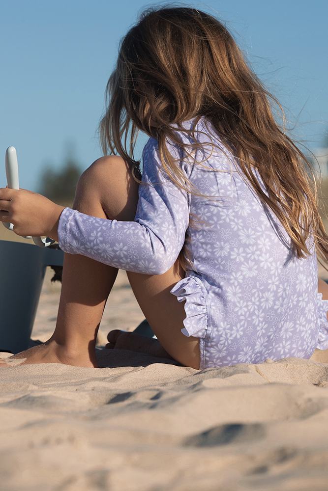 US stockist of Salty Swimwear's Zoe long sleeve rashsuit in Purple daisy days.  Made from purple UPF 50+ recycled Repreve fabric with pretty white daisy print. Fully lined, with invisible back zipper and signature Salty frill on legs.