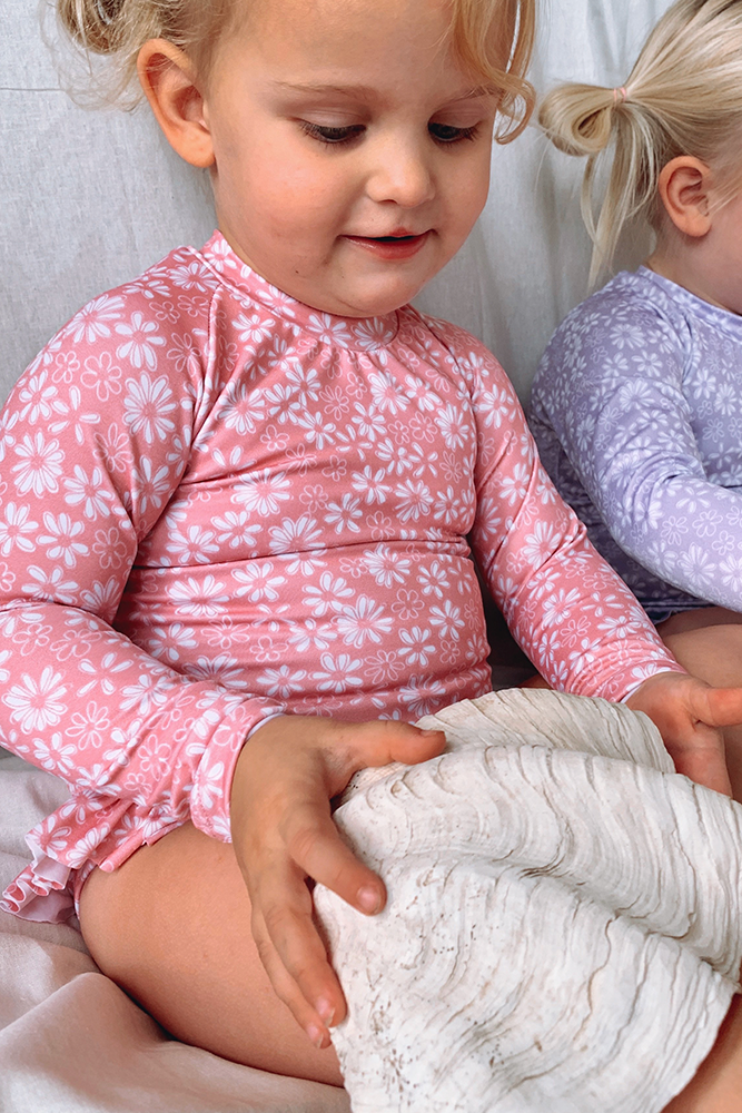 US stockist of Salty Swimwear's Zoe long sleeve rashsuit in pink daisy days.  Made from pink UPF 50+ recycled Repreve fabric with pretty white daisy print. Fully lined, with invisible back zipper and signature Salty frill on legs.