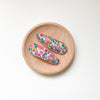 US stockist of Josie Joan's Abigail set of two fabric hair clips.  Cream colored fabric with red, pink, mustard and blue flowers.  Features scalloped edges.