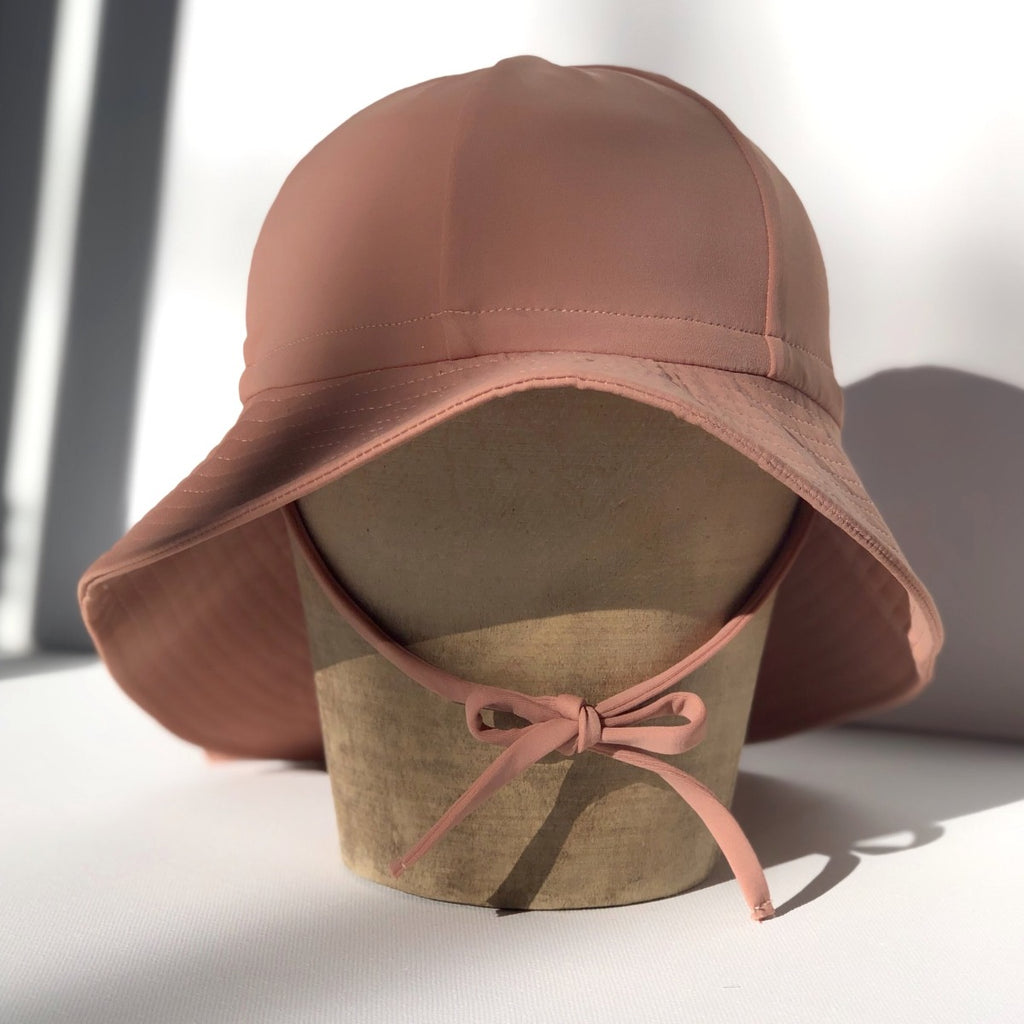 US stockist of Fini the Label's gender neutral, floppy swim hat in cocoa. Features elongated back for added sun protection, chin strap and adjustable bow around crown for better fit. Brim is medium stiffness and can be flipped up at front.  Made from nylon/spandex and is quick drying.