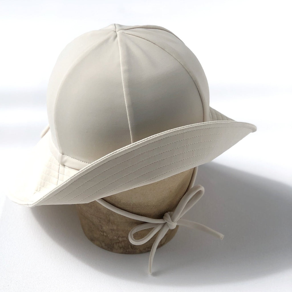 US stockist of Fini the Label's gender neutral, floppy swim hat in cream. Features elongated back for added sun protection, chin strap and adjustable bow around crown for better fit. Brim is medium stiffness and can be flipped up at front.  Made from nylon/spandex and is quick drying.