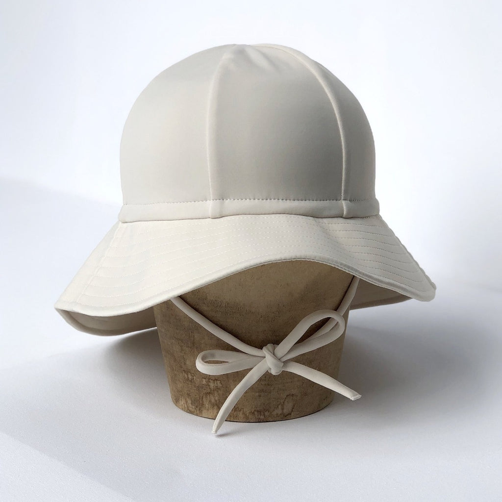 US stockist of Fini the Label's gender neutral, floppy swim hat in cream. Features elongated back for added sun protection, chin strap and adjustable bow around crown for better fit. Brim is medium stiffness and can be flipped up at front.  Made from nylon/spandex and is quick drying.