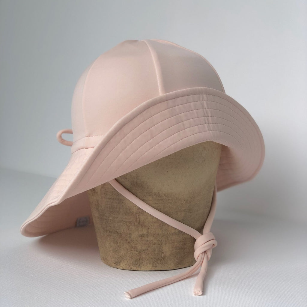 US stockist of Fini the Label's floppy swim hat in pale pink. Features elongated back for added sun protection, chin strap and adjustable bow around crown for better fit. Brim is medium stiffness and can be flipped up at front.  Made from nylon/spandex and is quick drying.