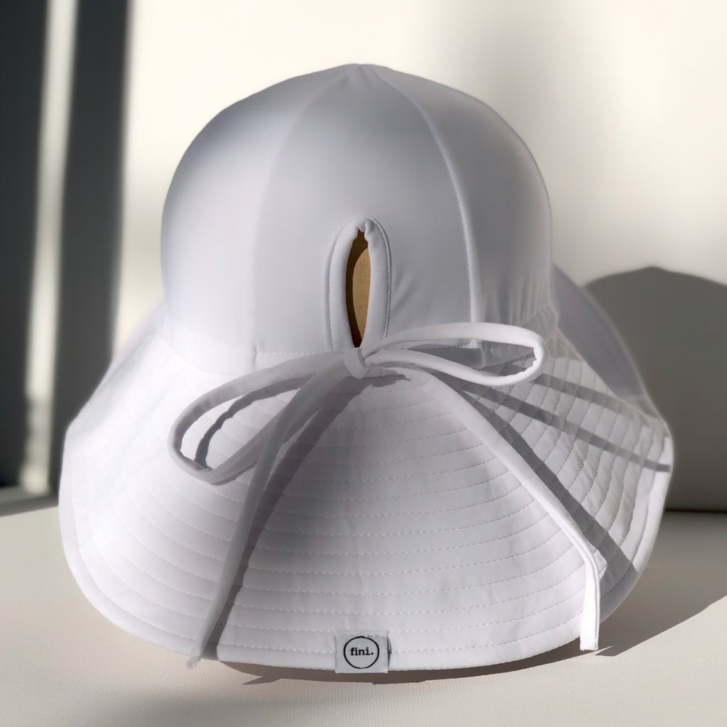 US stockist of Fini the Label's gender neutral floppy swim hat in white. Features elongated back for added sun protection, chin strap and adjustable bow around crown for better fit. Brim is medium stiffness and can be flipped up at front.  Made from nylon/spandex and is quick drying.