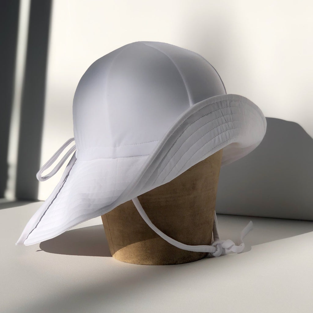 US stockist of Fini the Label's gender neutral floppy swim hat in white. Features elongated back for added sun protection, chin strap and adjustable bow around crown for better fit. Brim is medium stiffness and can be flipped up at front.  Made from nylon/spandex and is quick drying.