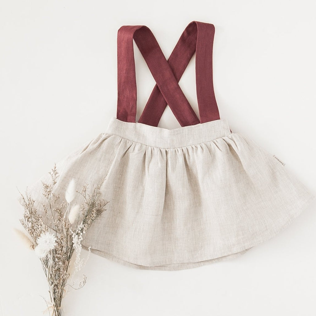 US stockist of Karibou Kid's Coco Linen Suspender Skirt in the Frosted Cherry Edition.  Features natural linen skirt with contrasting mauve suspender straps and bows on back.