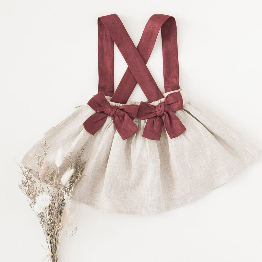 US stockist of Karibou Kid's Coco Linen Suspender Skirt in the Frosted Cherry Edition.  Features natural linen skirt with contrasting mauve suspender straps and bows on back.