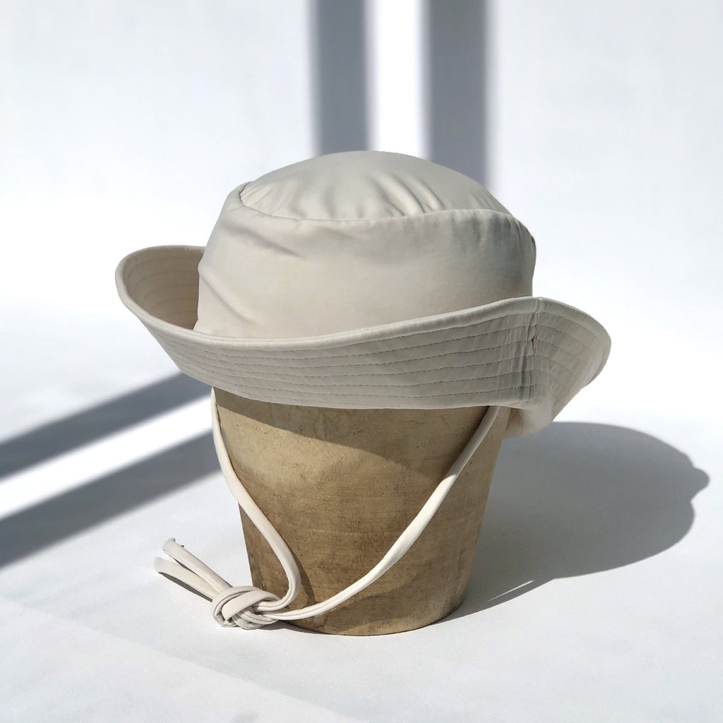 US stockist of Fini the Label's gender neutral, sailor swim hat in cream. Features elongated back for added sun protection, wide brim and chin strap. Brim is medium stiffness and can be flipped up at front. Sides can be worn buttoned up for that sailor look.  Made from nylon/spandex and is quick drying.
