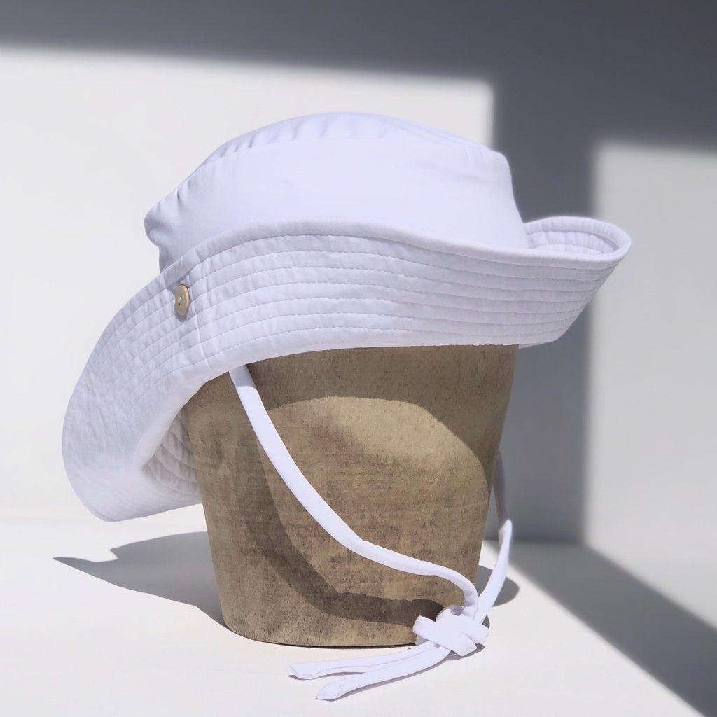 US stockist of Fini the Label's gender neutral, sailor swim hat in white. Features elongated back for added sun protection, wide brim and chin strap. Brim is medium stiffness and can be flipped up at front. Sides can be worn buttoned up for that sailor look.  Made from nylon/spandex and is quick drying.