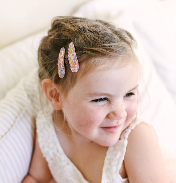 US stockist of Josie Joan's Amelia fabric hair clips.  Set of two fabric hair clips made from pale coloured fabric with multicolored flowers and  contrasting blue leaves.  Has scalloped edging.