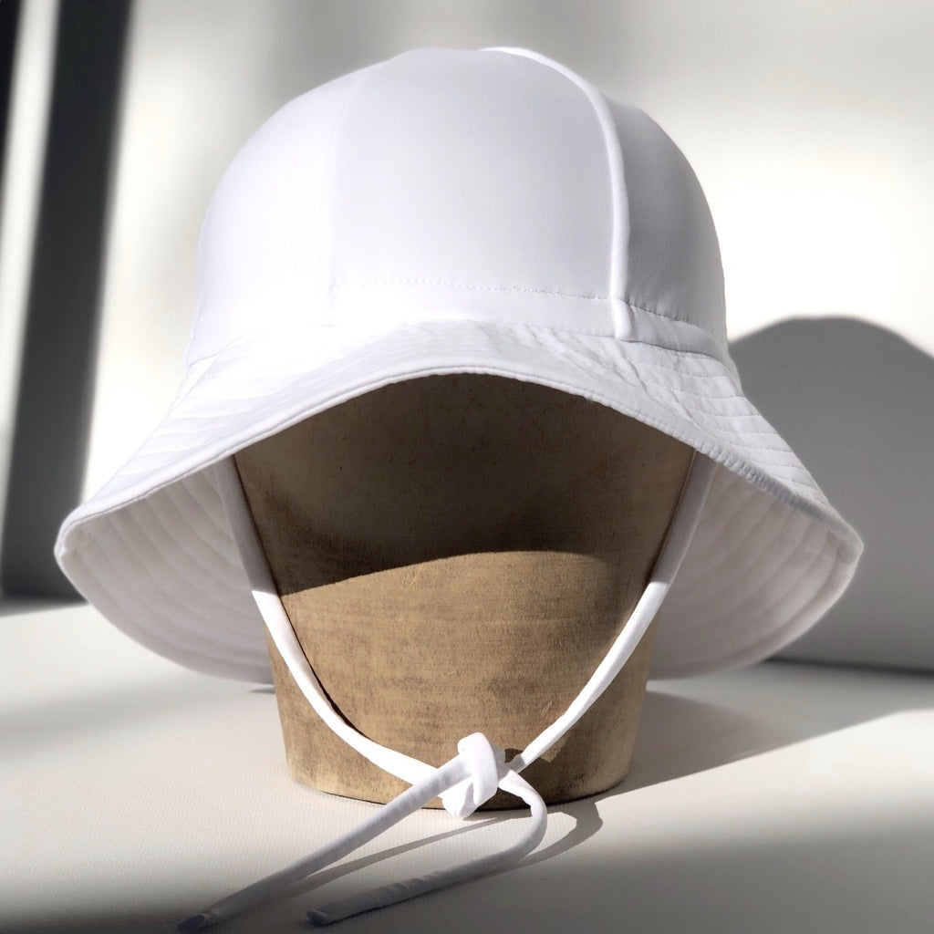 US stockist of Fini the Label's gender neutral floppy swim hat in white. Features elongated back for added sun protection, chin strap and adjustable bow around crown for better fit. Brim is medium stiffness and can be flipped up at front.  Made from nylon/spandex and is quick drying.