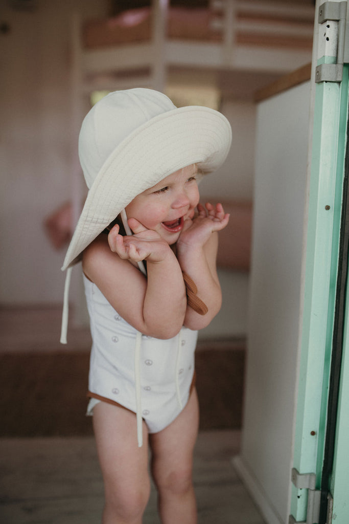 US stockist of Fini the Label's gender neutral, floppy swim hat in cream. Features elongated back for added sun protection, chin strap and adjustable bow around crown for better fit. Brim is medium stiffness and can be flipped up at front.  Made from nylon/spandex and is quick drying.