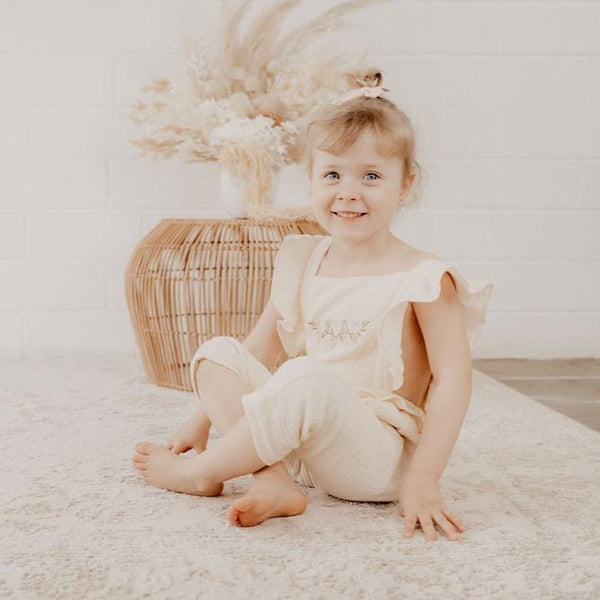 US stockist of India and Grace the Label's cream embroidered ruffle jumpsuit.  Features ruffle straps that cross over the back, floral embroidery on the chest, ruffle at waist and 3/4 legs.  Made from double cotton gauze.