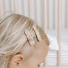 US stockist of Josie Joan's Little Audrey fabric baby hair clips.  Set of two fabric hair clips made from pale coloured fabric with bright orange, purple, red, yellow or pink flowers and  contrasting green leaves.  Has scalloped edging.