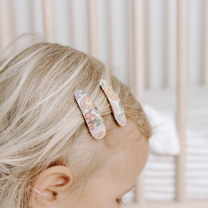 US stockist of Josie Joan's Little Audrey fabric baby hair clips.  Set of two fabric hair clips made from pale coloured fabric with bright orange, purple, red, yellow or pink flowers and  contrasting green leaves.  Has scalloped edging.