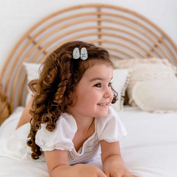 US stockist of Josie Joan's Suzanne set of two fabric hair clips.  Pale colored fabric with pastel flowers in hues of pink, purple, blue and yellow. Features scalloped edges.