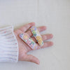 US stockist of Josie Joan's Little Audrey fabric baby hair clips.  Set of two fabric hair clips made from pale coloured fabric with bright orange, purple, red, yellow or pink flowers and  contrasting green leaves.  Has scalloped edging.