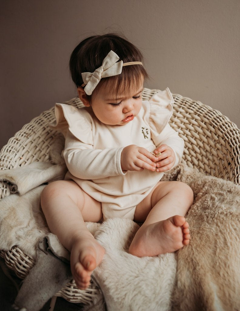 US stockist of Karibou Kid's Milana Winged Playsuit in almond cream.  Made from soft cotton, featuring long sleeves and ruffled wings at shoulders.